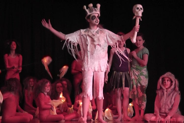 A white king wearing a crown of bones surrounded by fire dancers