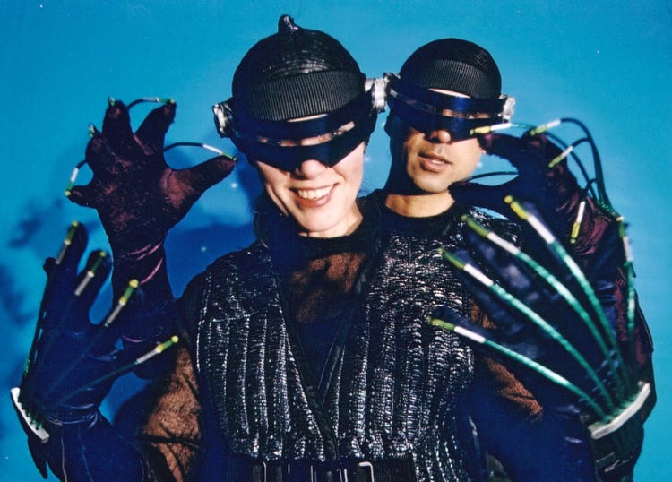 Nem and Jax geared up for a ride into virtual reality, wearing visors and gloves with wiring along each finger.
