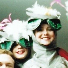 Two girls smiling from under masks with enormous green eyes and feathered heads.