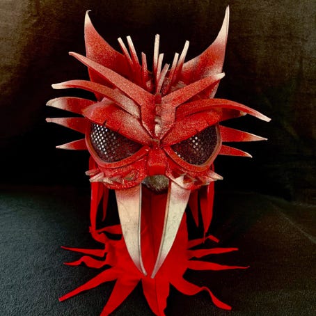 A spikey full-head red mask with large black eyes and two long, fangs.