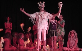 A white king wearing a crown of bones surrounded by fire dancers
