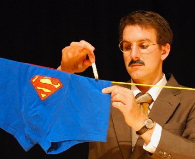 Sam in a beige suit and tie, pegging his Superman underwear on the washing line.