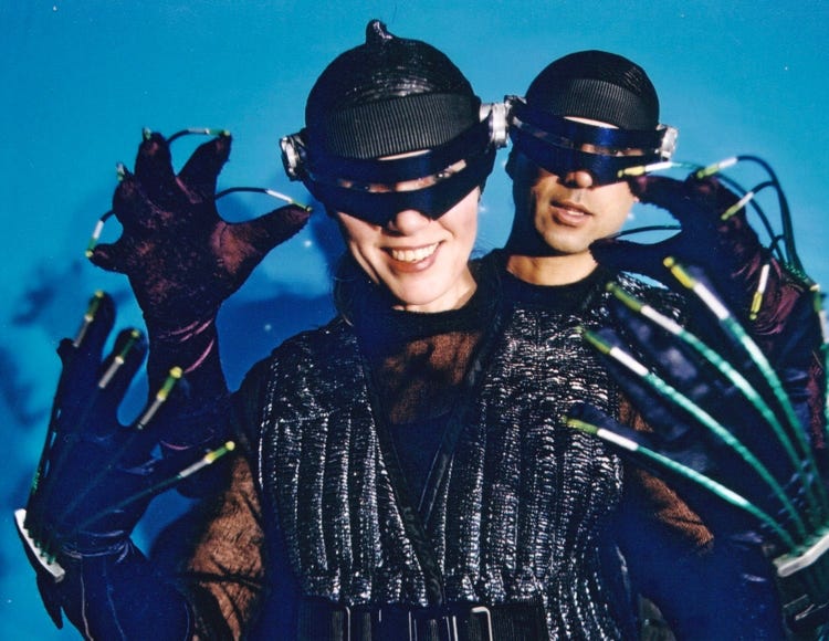 Nem and Jax geared up for a ride into virtual reality, wearing visors and gloves with wiring along each finger.