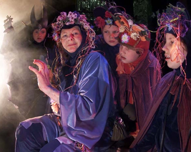 A woman wearing a floral headband, children wearing Woodlander costumes and a boy clad in black with a claw for a hand.